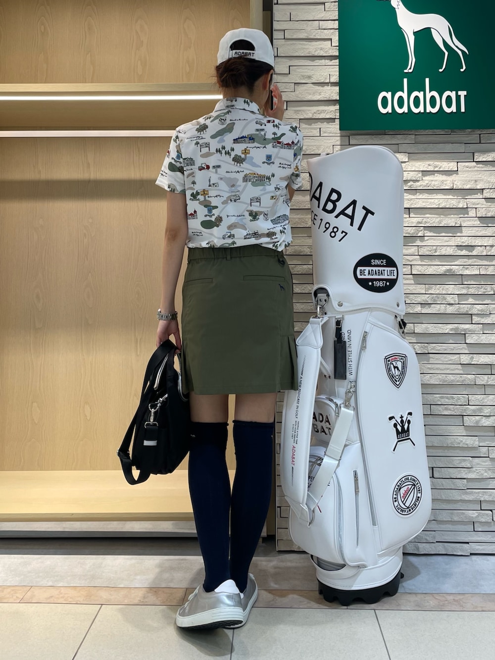 グリーン系のスカート、グリーン系のポロシャツ、ブラック系のハンドバッグを着用したレディースの秋コーディネートの3枚目の写真