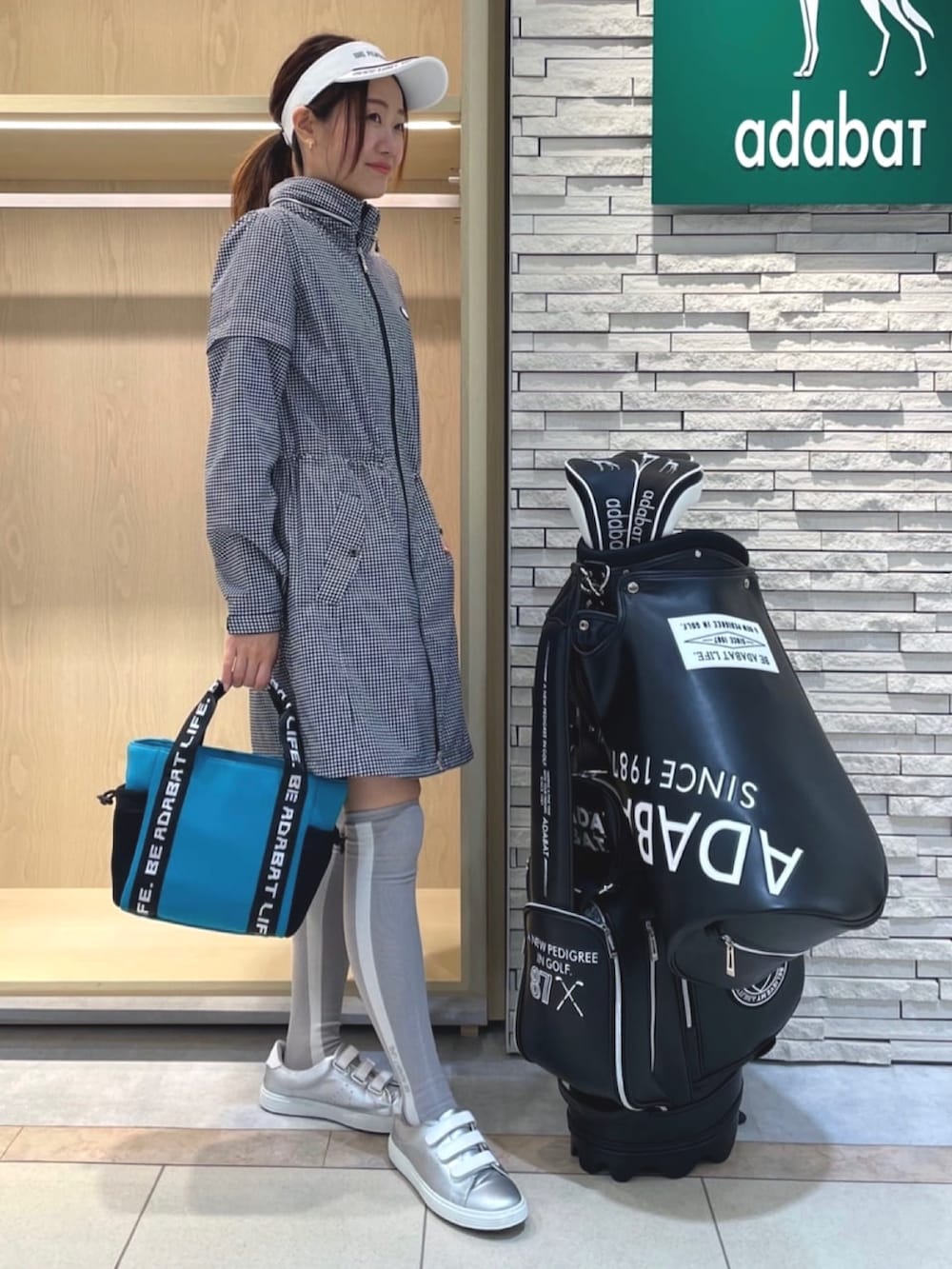 ブルー系のトートバッグ、ホワイト系のブルゾン、ホワイト系のサンバイザーを着用したレディースの夏コーディネートの2枚目の写真