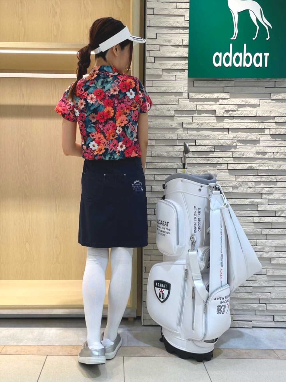 ブルー系のスカート、ピンク系のポロシャツ、ホワイト系のサンバイザーを着用したレディースの夏コーディネートの3枚目の写真