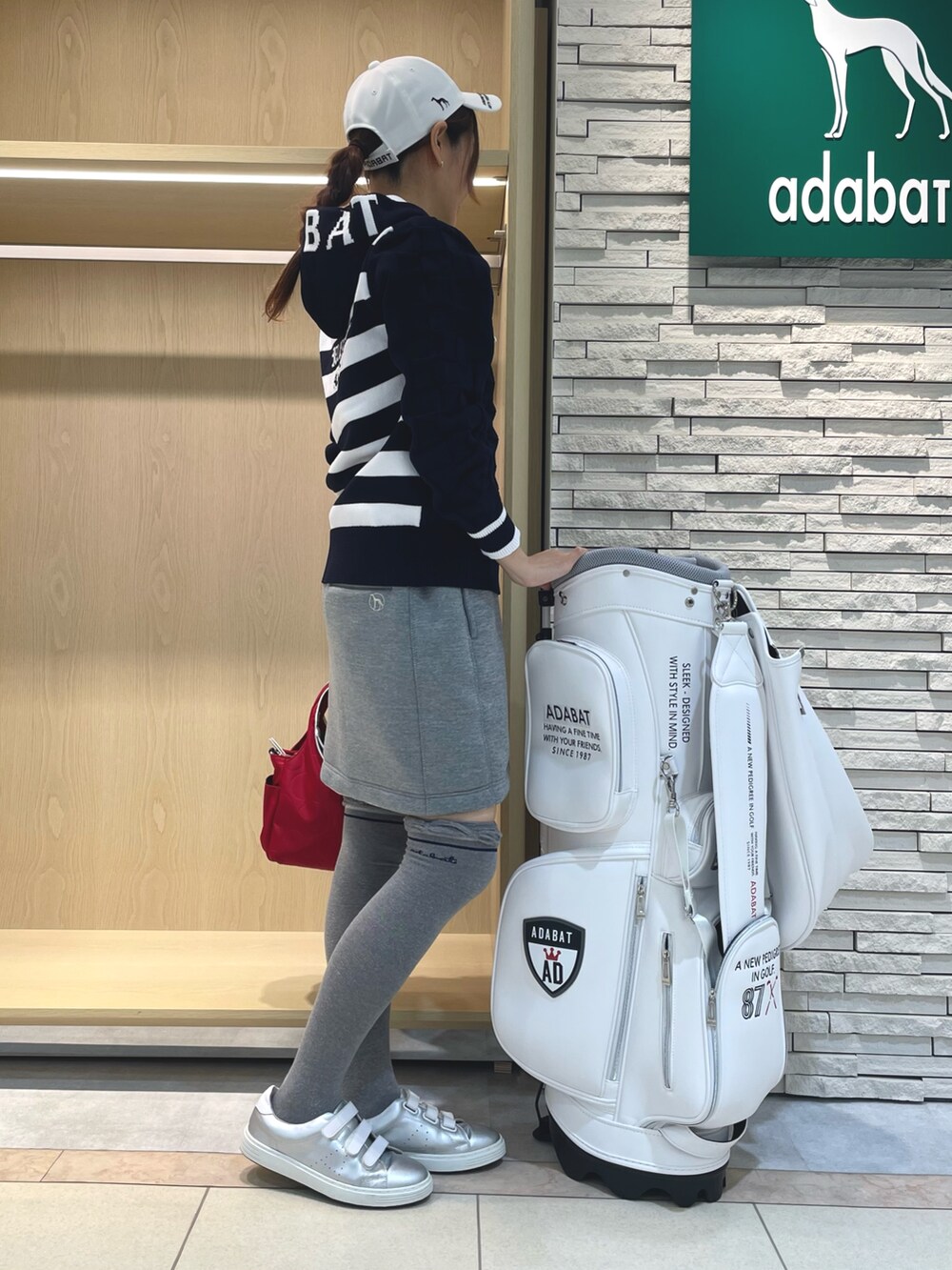 グレー系のスカート、ブルー系のニット/セーター、レッド系のハンドバッグを着用したレディースの秋コーディネートの3枚目の写真