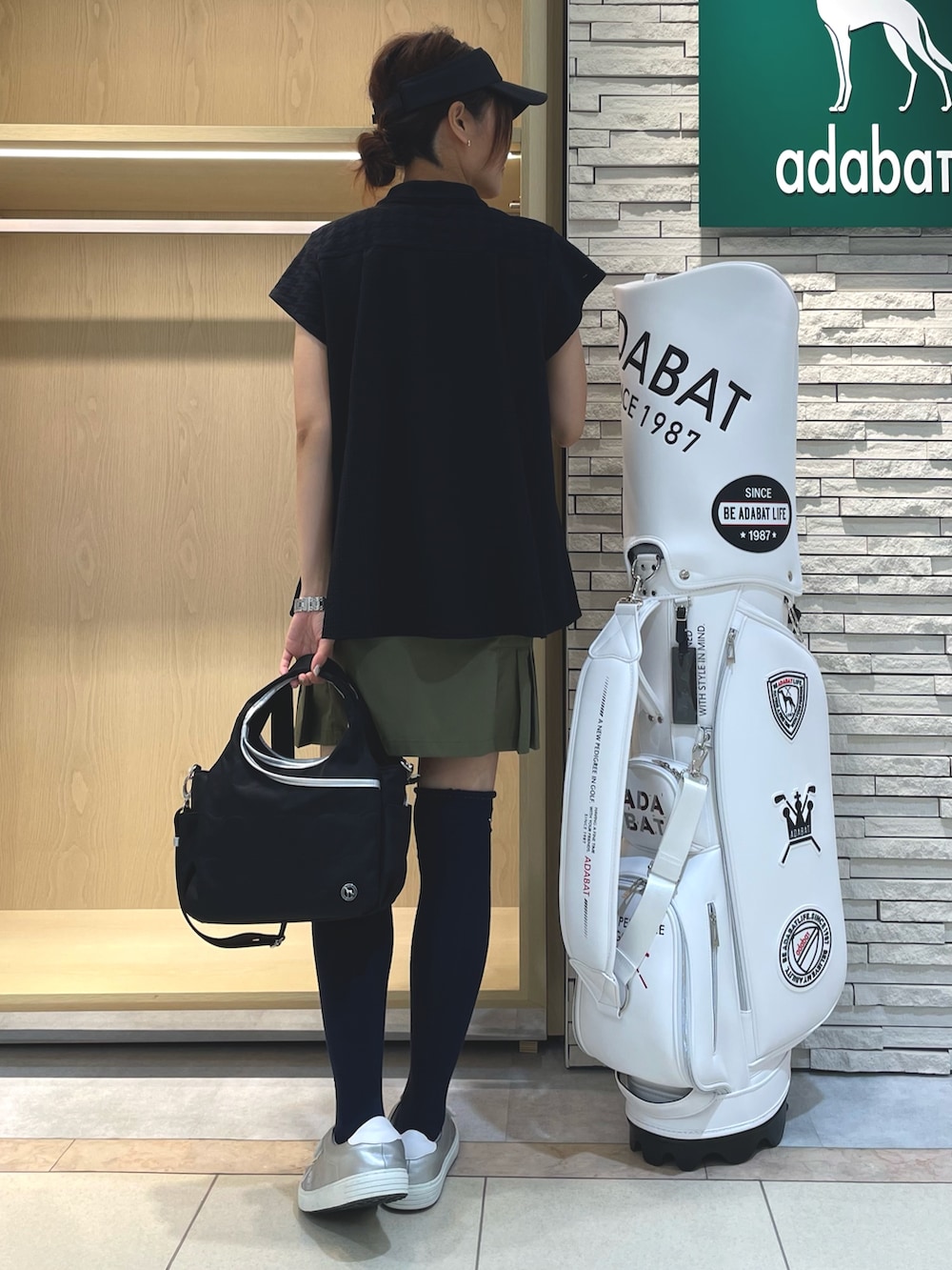 ブラック系のポロシャツ、グリーン系のスカート、ブラック系のハンドバッグを着用したレディースの秋コーディネートの3枚目の写真