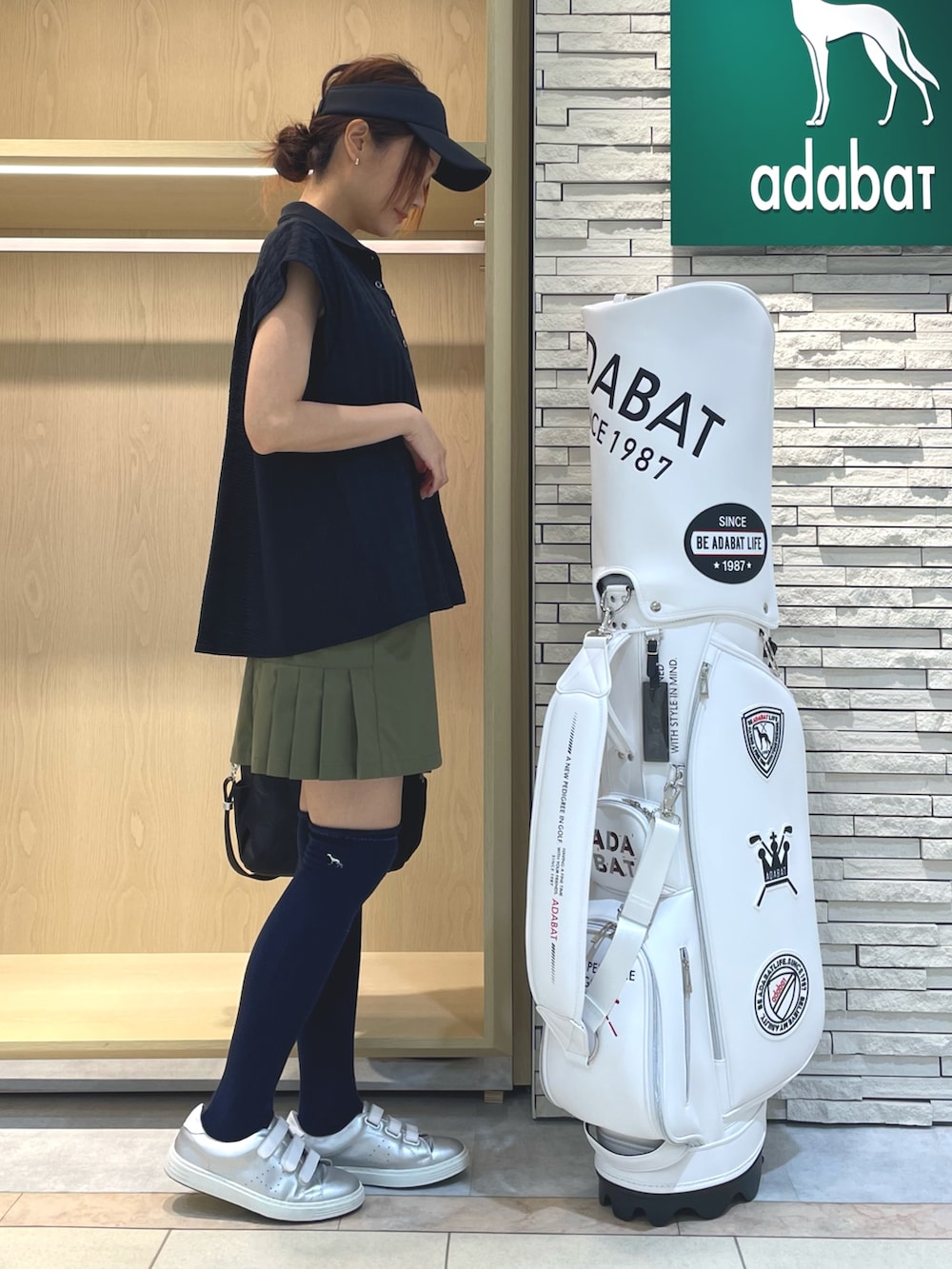 ブラック系のポロシャツ、グリーン系のスカート、ブラック系のハンドバッグを着用したレディースの秋コーディネートの2枚目の写真