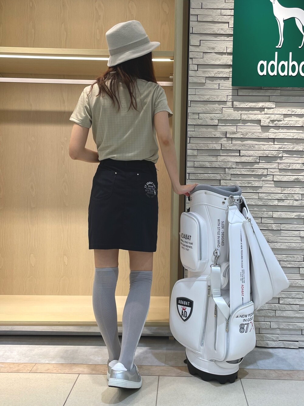 ブラック系のスカート、ベージュ系のポロシャツ、ベージュ系のハットを着用したレディースの夏コーディネートの4枚目の写真