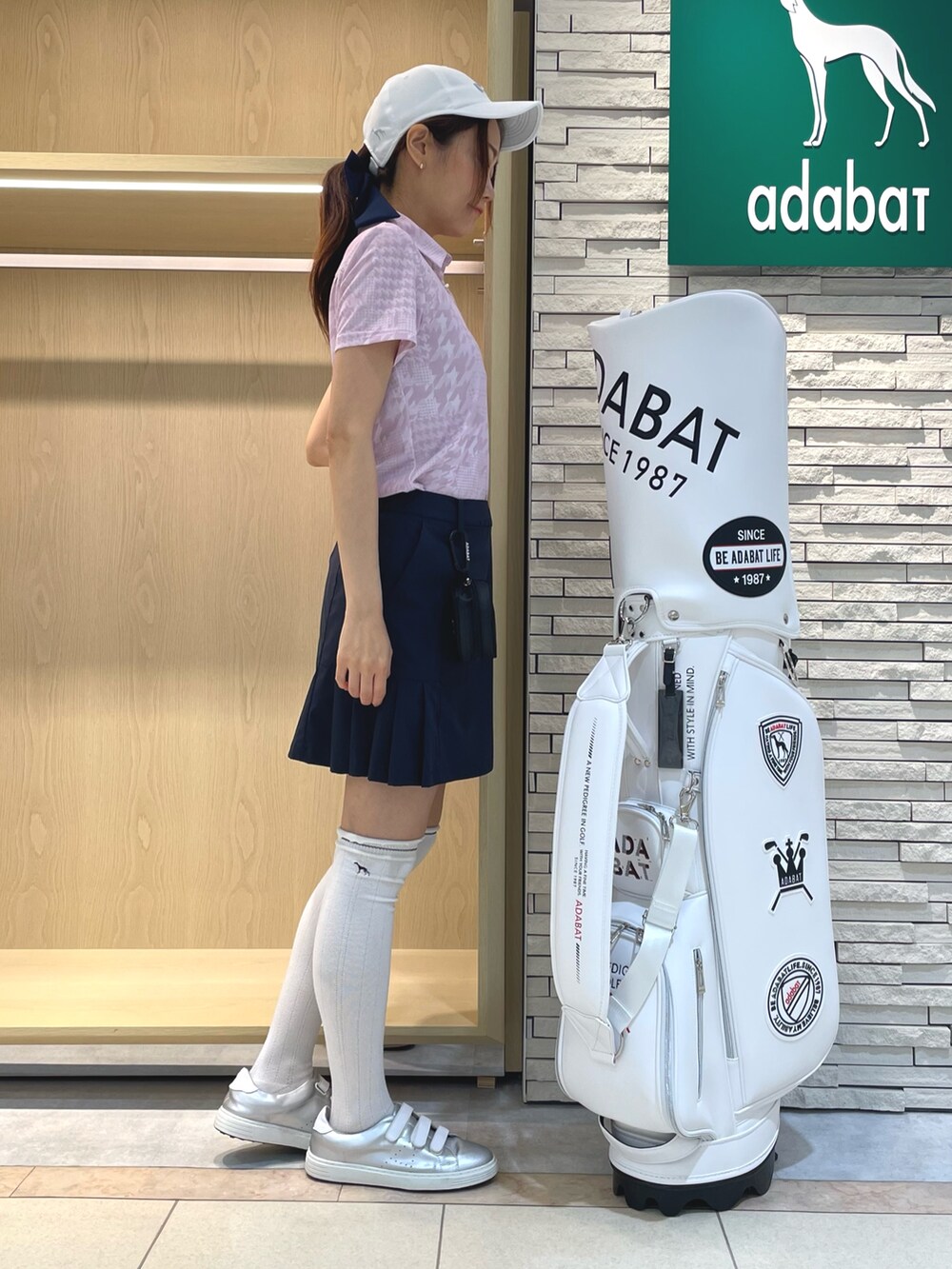 ピンク系のポロシャツ、ブルー系のスカート、ホワイト系のキャップを着用したレディースの夏コーディネートの2枚目の写真