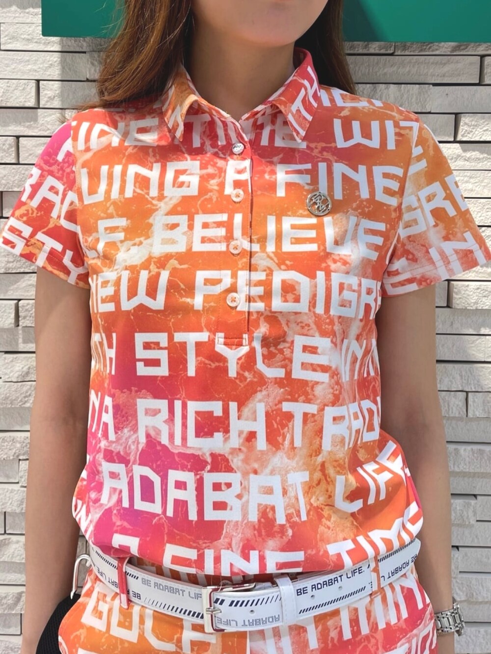 オレンジ系のポロシャツ、オレンジ系のトートバッグ、ホワイト系のキャップを着用したレディースの夏コーディネートの4枚目の写真