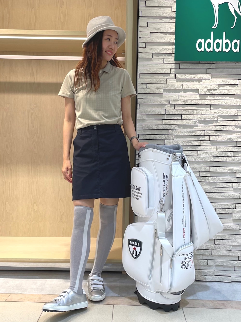 ブラック系のスカート、ベージュ系のポロシャツ、ベージュ系のハットを着用したレディースの夏コーディネートの2枚目の写真