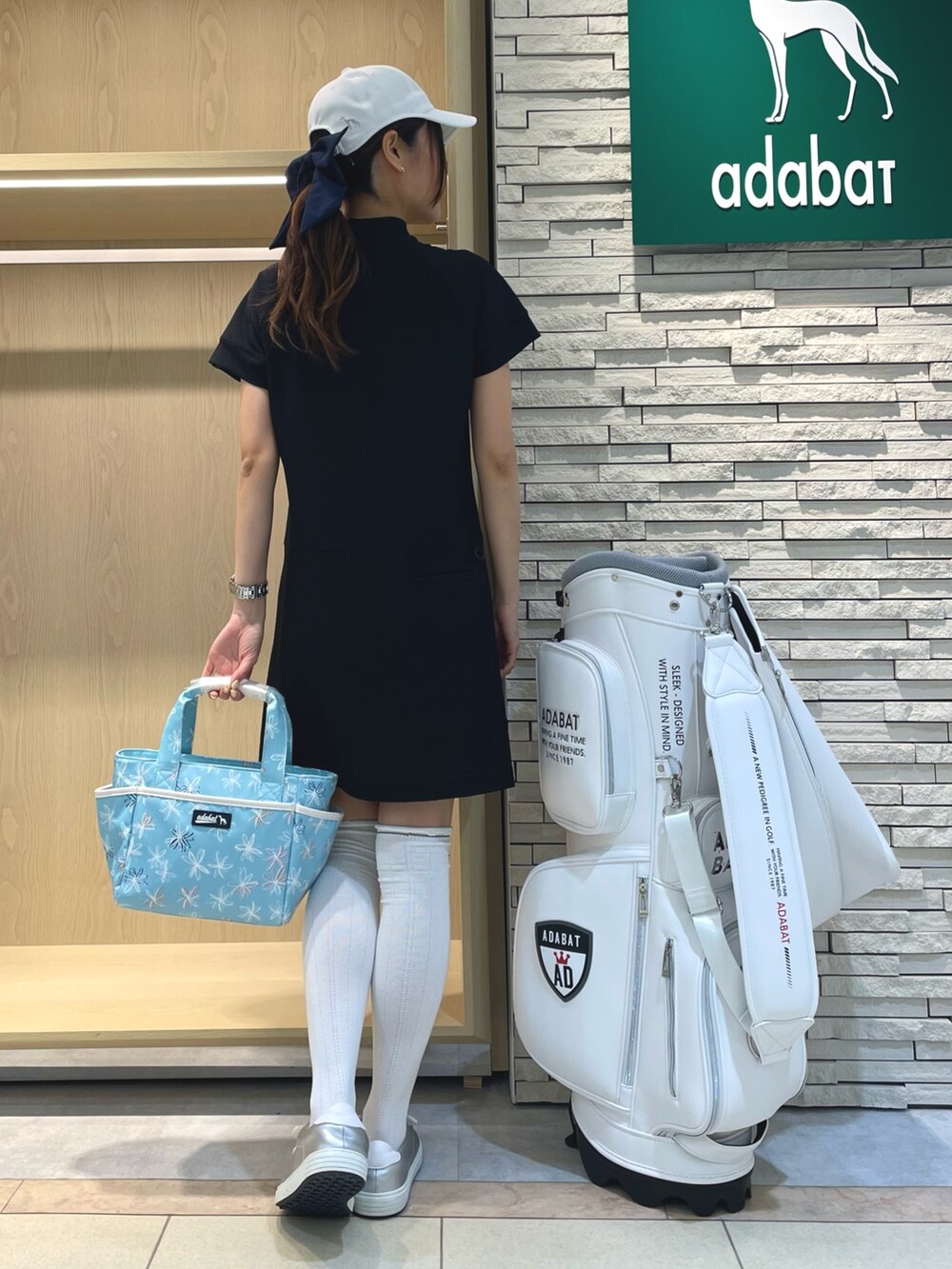 ブラック系のワンピース、ブルー系のハンドバッグ、ホワイト系のキャップを着用したレディースの春コーディネートの2枚目の写真