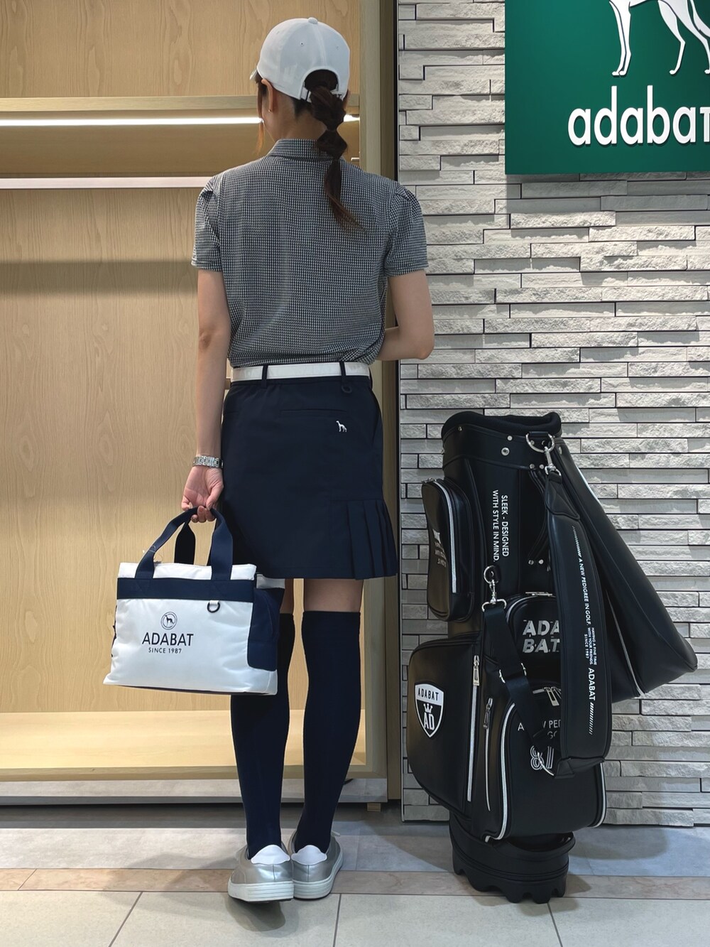 ブラック系のポロシャツ、ブルー系のスカート、ホワイト系のキャップを着用したレディースの夏コーディネートの2枚目の写真