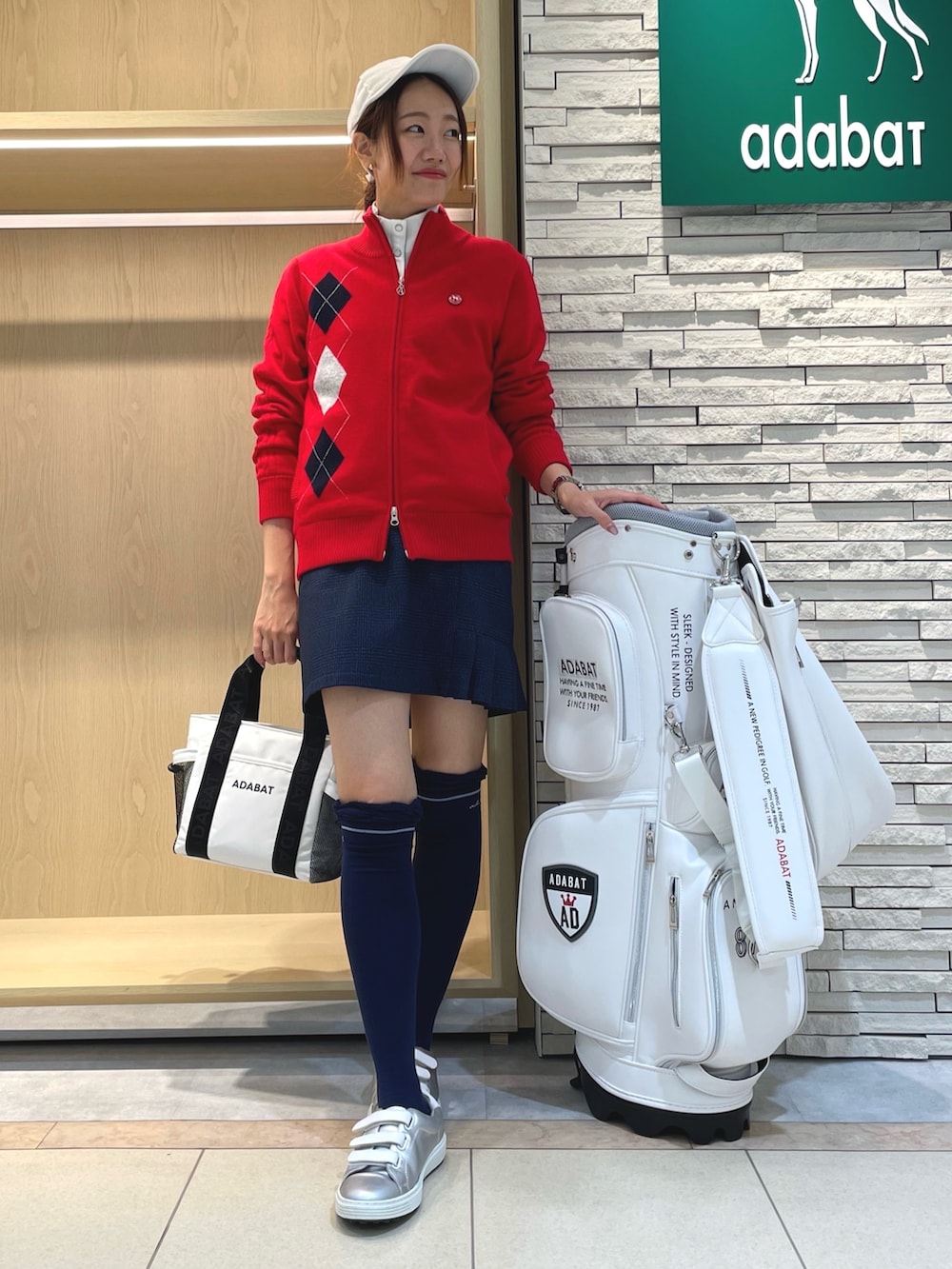 ブルー系のスカート、ホワイト系のトートバッグ、レッド系のニット/セーターを着用したレディースの秋コーディネートの2枚目の写真