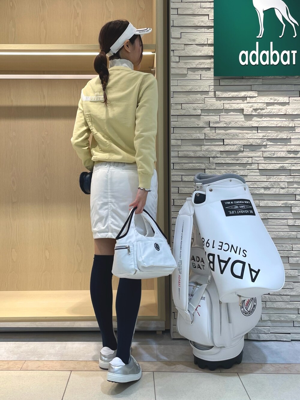 イエロー系のニット/セーター、ホワイト系のトートバッグ、グリーン系のスカートを着用したレディースの冬コーディネートの2枚目の写真