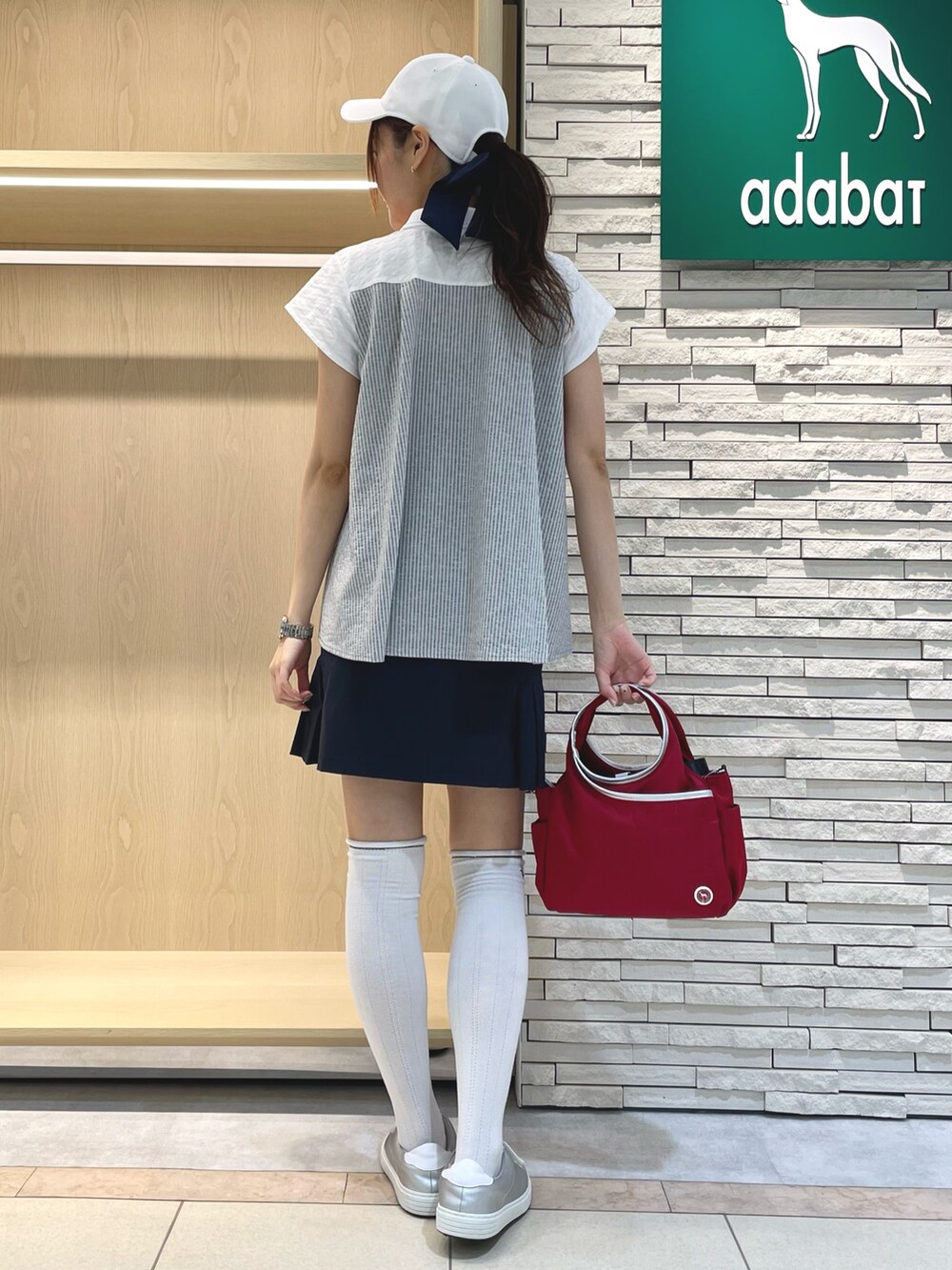 ブルー系のスカート、ホワイト系のポロシャツ、レッド系のハンドバッグを着用したレディースの秋コーディネートの3枚目の写真