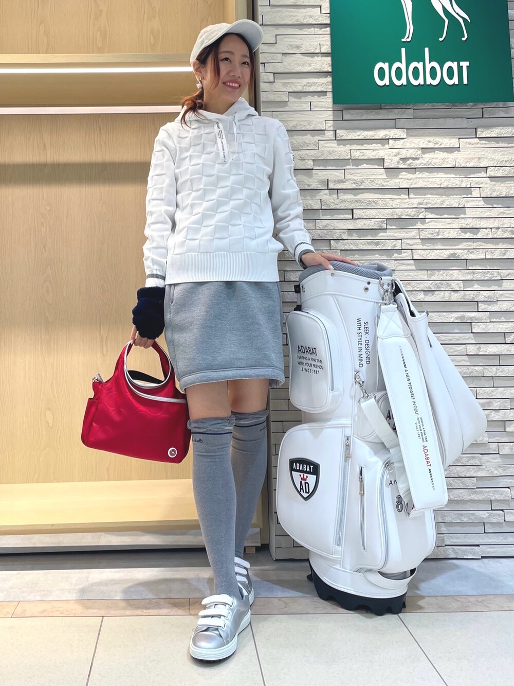 グレー系のスカート、ホワイト系のニット/セーター、レッド系のハンドバッグを着用したレディースの秋コーディネートの2枚目の写真