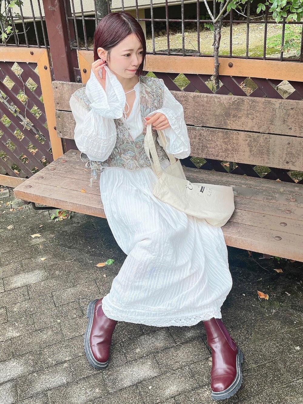 レッド系のブーツ、グリーン系のベスト、ホワイト系のワンピースを着用したレディースの冬コーディネートの2枚目の写真