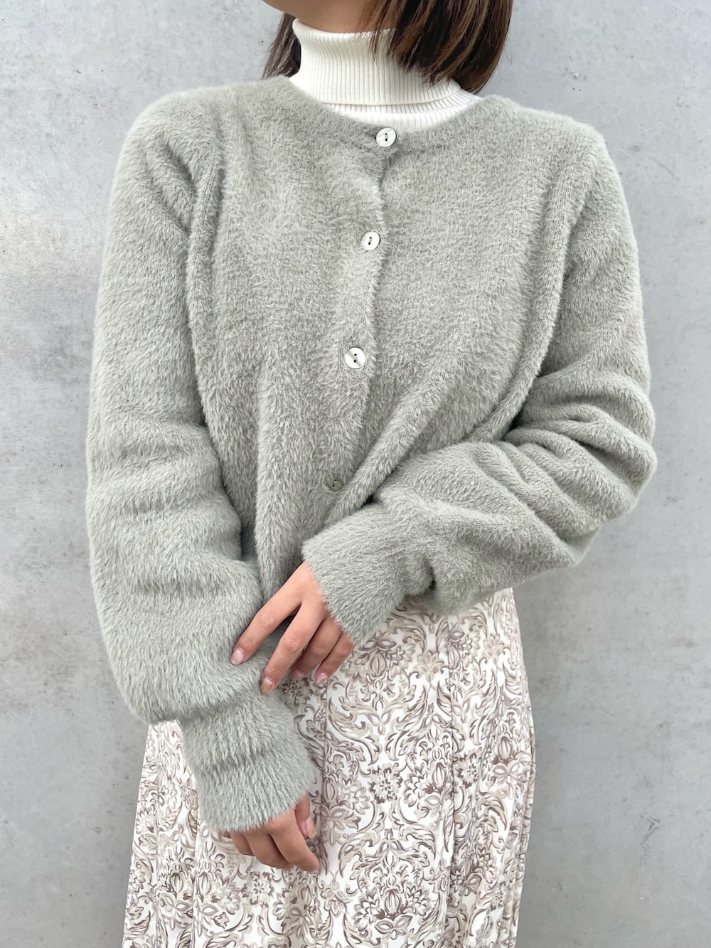 グリーン系のカーディガン/ボレロ、ホワイト系のスカート、ホワイト系のブーツを着用したレディースの冬コーディネートの2枚目の写真