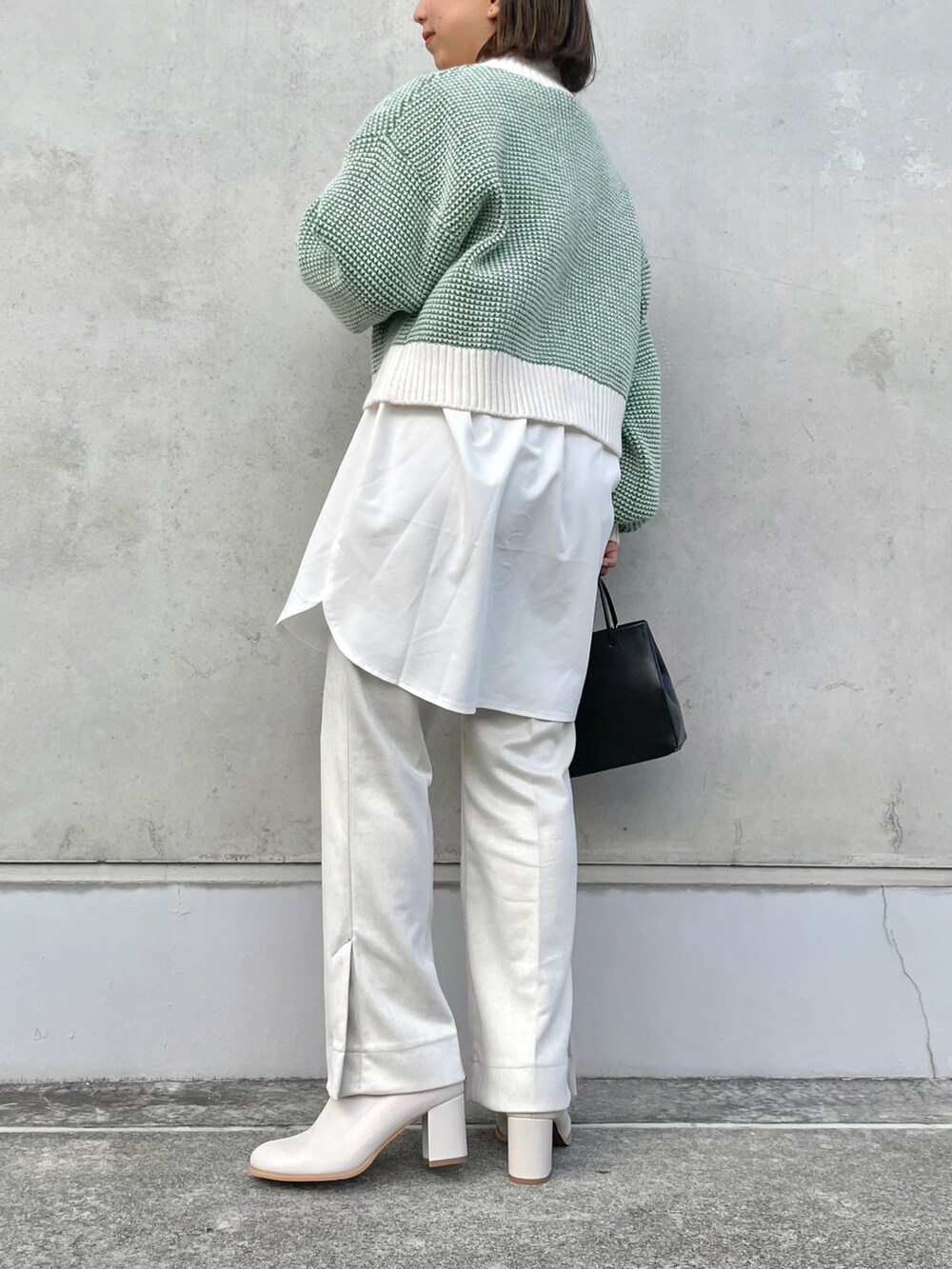 グリーン系のニット/セーター、ブラック系のトートバッグ、ホワイト系のスラックスを着用したレディースの冬コーディネートの2枚目の写真