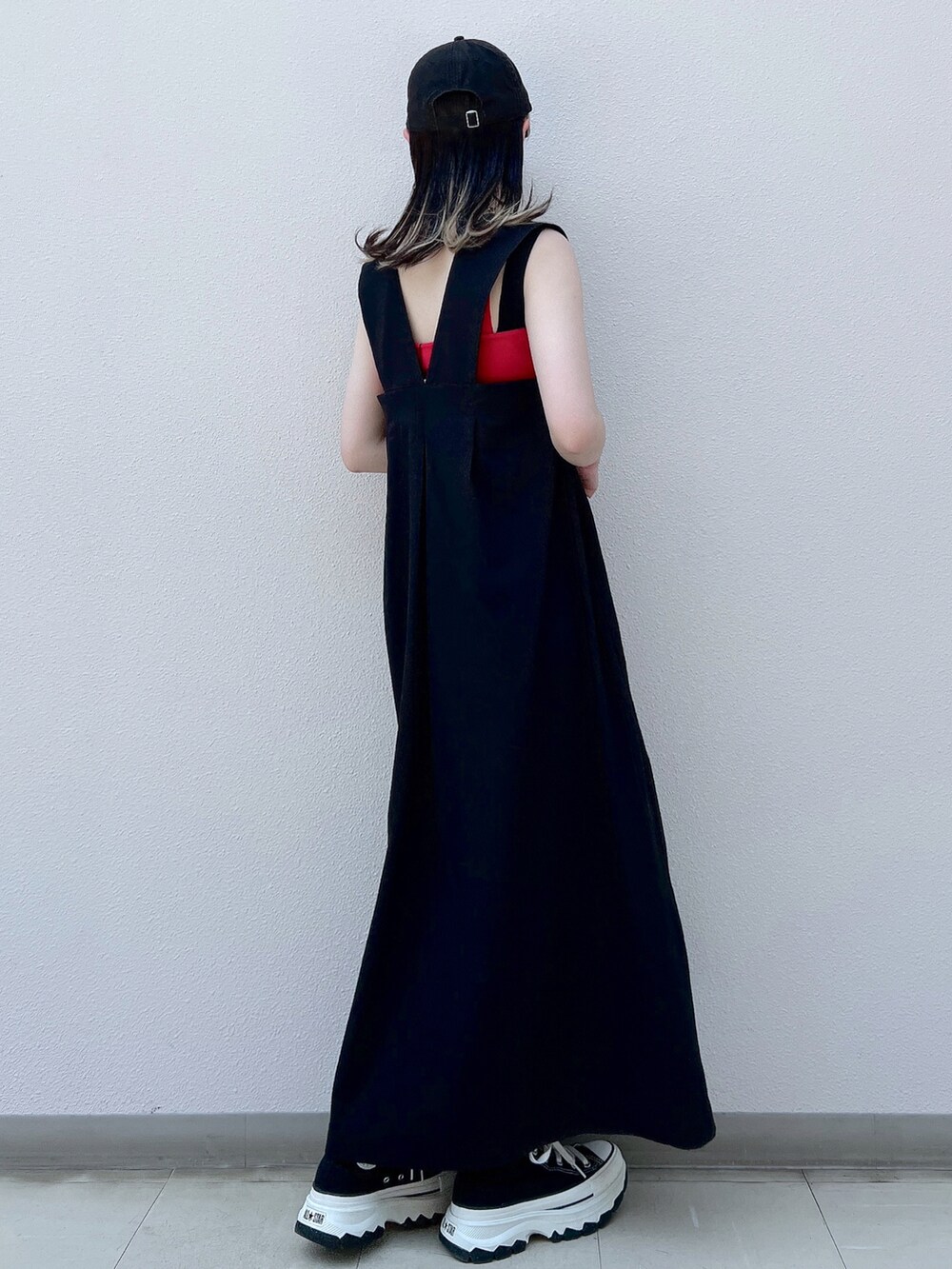 ブラック系のジャンパースカート、レッド系のタンクトップ、ブラック系のスニーカーを着用したレディースの春コーディネートの2枚目の写真