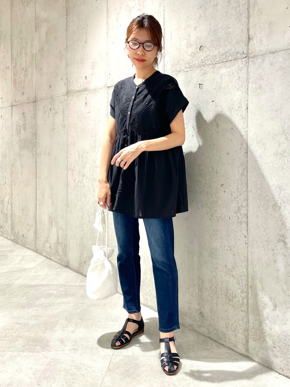 ブラック系のサンダル、ブルー系のデニムパンツ、ホワイト系のショルダーバッグを着用したレディースの夏コーディネートの2枚目の写真