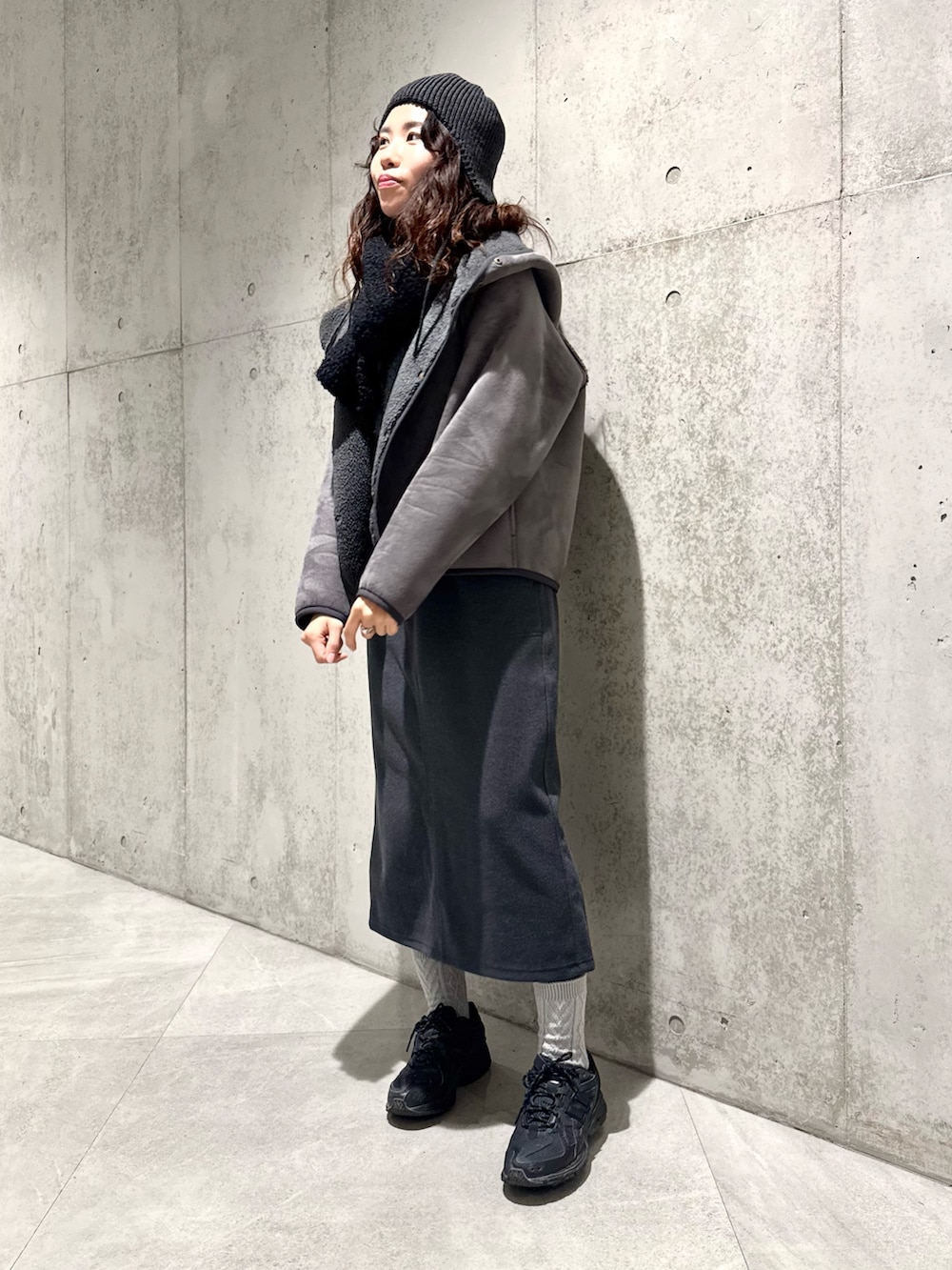 ブラック系のムートンコート、グレー系のニット/セーター、グレー系のスカートを着用したレディースの冬コーディネートの2枚目の写真