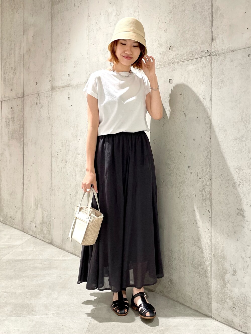 ホワイト系のかごバッグ、ブラック系のスカート、ホワイト系のTシャツ/カットソーを着用したレディースの夏コーディネートの2枚目の写真