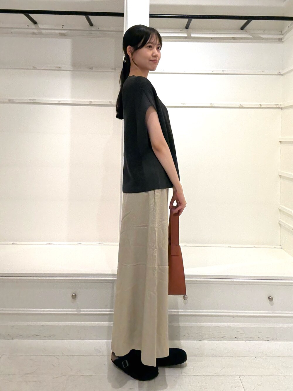 ブラウン系のハンドバッグ、グレー系のニット/セーター、ベージュ系のスカートを着用したレディースの夏コーディネートの2枚目の写真