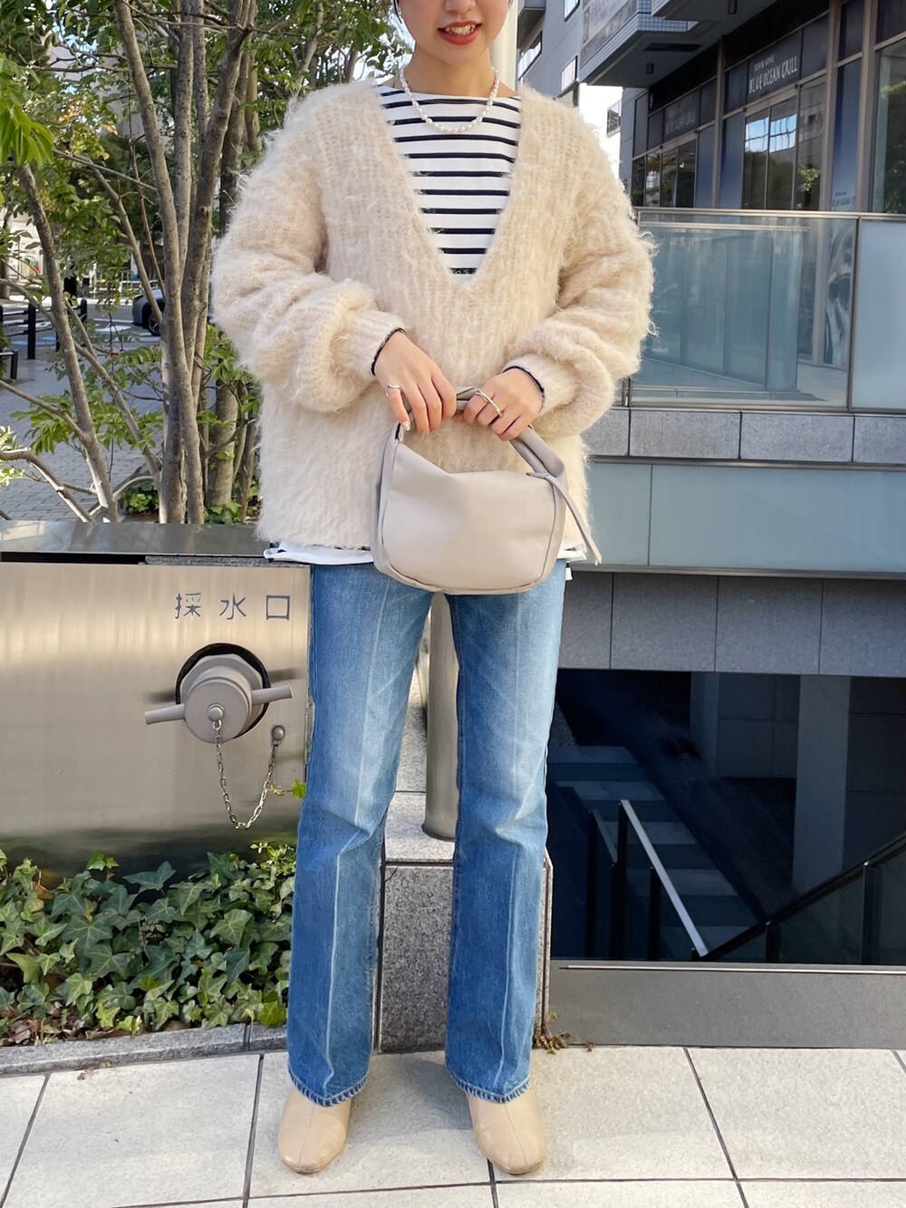 ブルー系のデニムパンツ、ベージュ系のハンドバッグ、ベージュ系のニット/セーターを着用したレディースの冬コーディネートの4枚目の写真