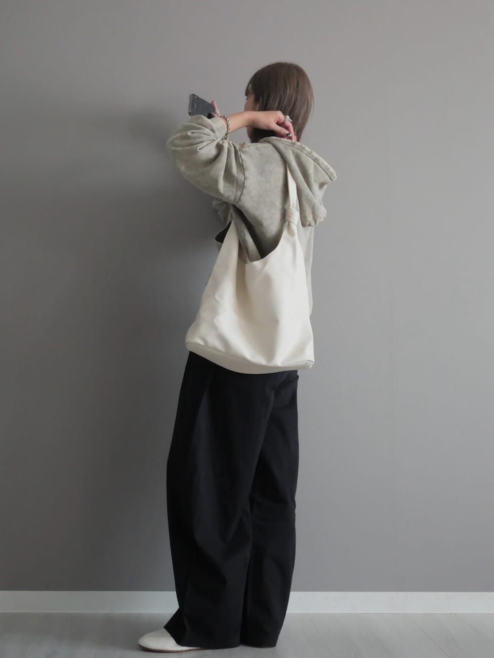 グレー系のパーカー、ホワイト系のトートバッグ、ブラック系のチノパンツを着用したレディースの秋コーディネートの4枚目の写真