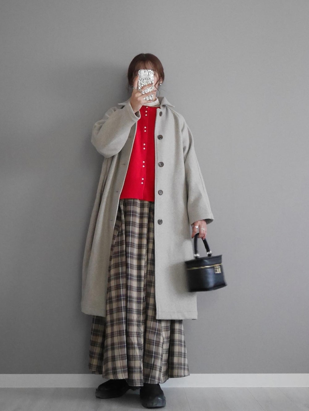 ベージュ系のステンカラーコート、レッド系のカーディガン/ボレロ、ベージュ系のスカートを着用したレディースの秋コーディネートの2枚目の写真