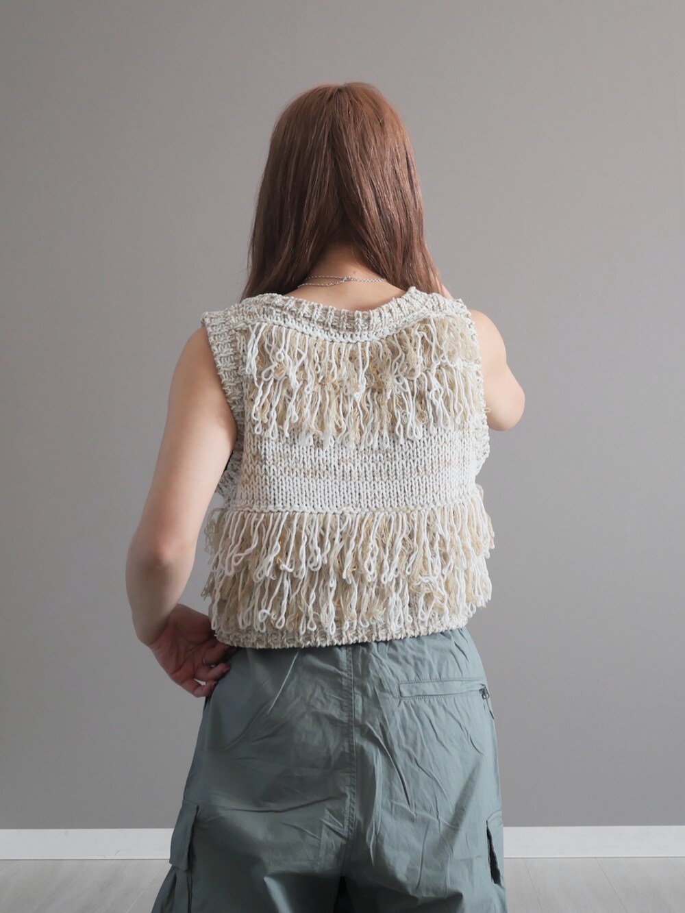 ホワイト系のベスト、グリーン系のパンツ、ブラック系のショルダーバッグを着用したレディースの春コーディネートの3枚目の写真