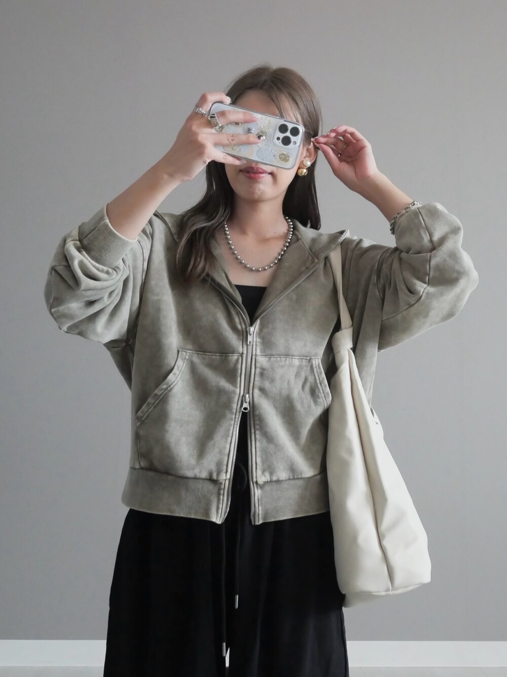 グレー系のパーカー、ホワイト系のトートバッグ、ブラック系のチノパンツを着用したレディースの秋コーディネートの2枚目の写真