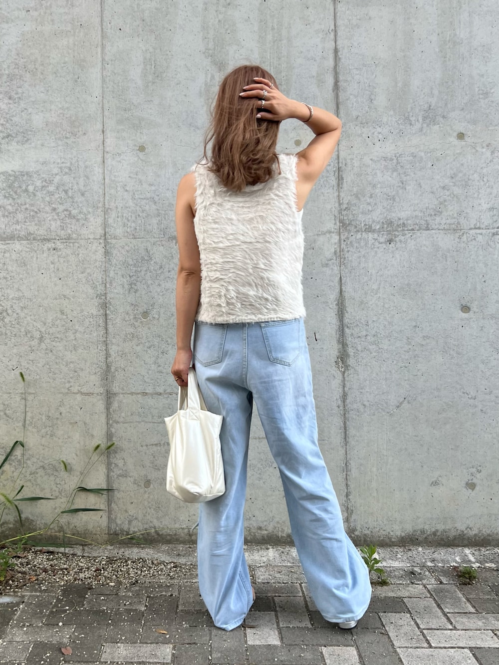 グレー系のベスト、ブルー系のデニムパンツ、ホワイト系のハンドバッグを着用したレディースの秋コーディネートの3枚目の写真