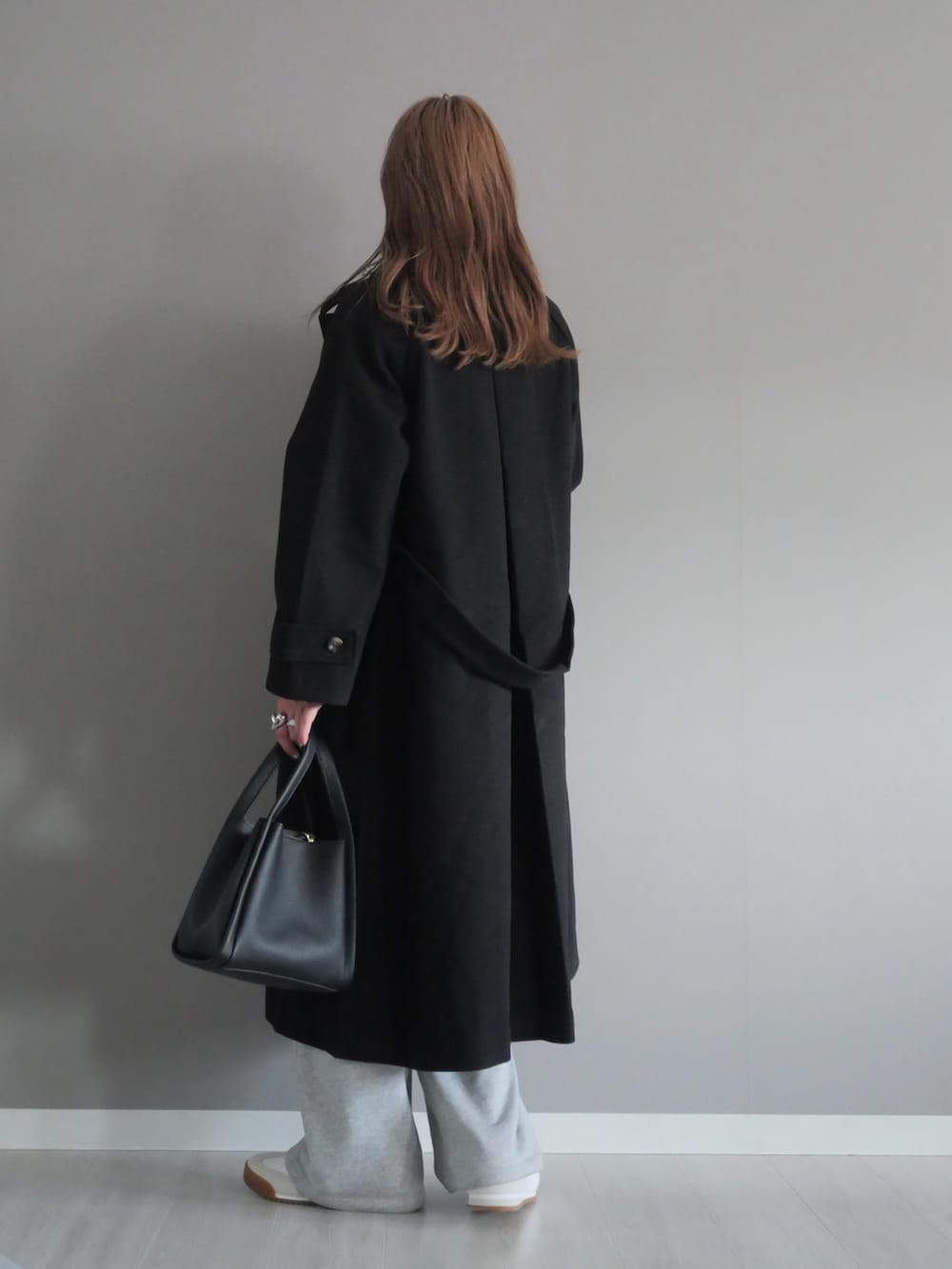 ブラック系のステンカラーコート、グレー系のスウェットパンツ、ブラック系のハンドバッグを着用したレディースの秋コーディネートの3枚目の写真