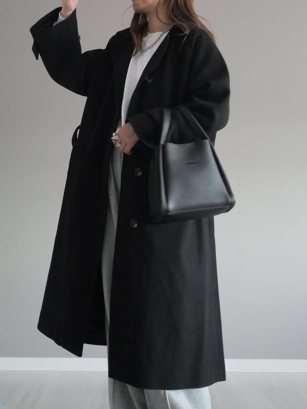 ブラック系のステンカラーコート、グレー系のスウェットパンツ、ブラック系のハンドバッグを着用したレディースの秋コーディネートの2枚目の写真