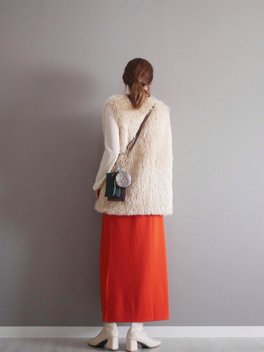 ホワイト系のベスト、オレンジ系のスカート、ブラウン系のショルダーバッグを着用したレディースの秋コーディネートの2枚目の写真