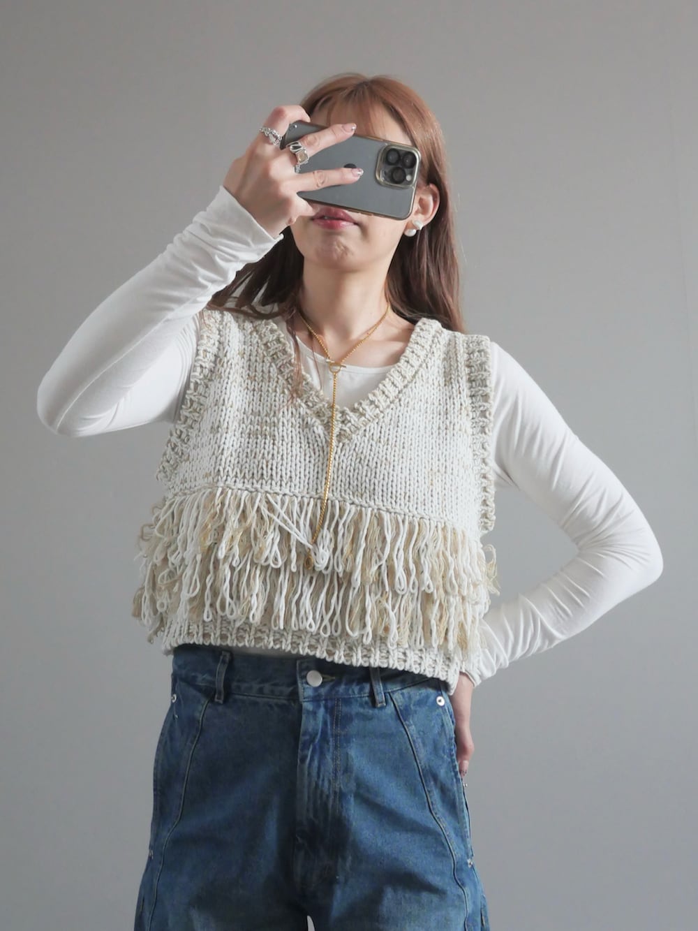 ホワイト系のベスト、ブルー系のデニムパンツ、ホワイト系のハンドバッグを着用したレディースの春コーディネートの2枚目の写真