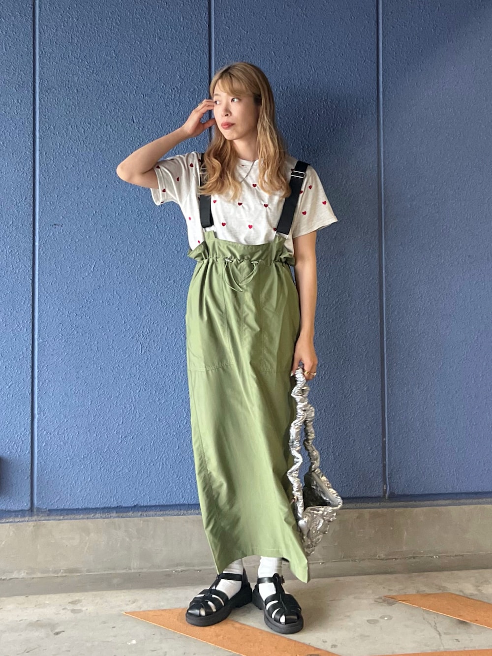 グリーン系のジャンパースカート、ベージュ系のTシャツ/カットソー、シルバー系のハンドバッグを着用したレディースの夏コーディネートの2枚目の写真