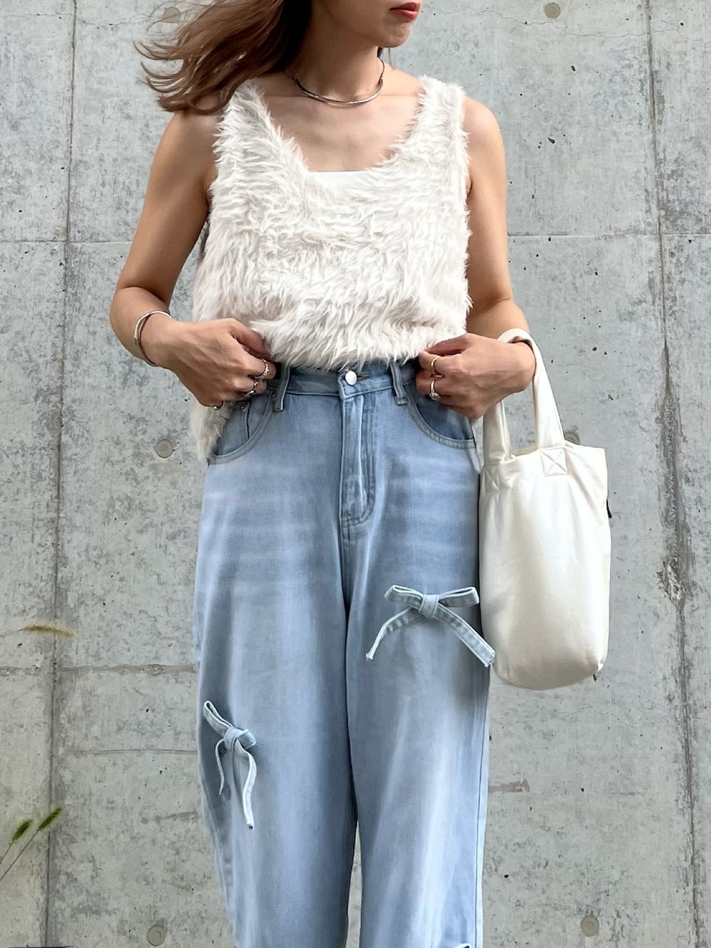 グレー系のベスト、ブルー系のデニムパンツ、ホワイト系のハンドバッグを着用したレディースの秋コーディネートの2枚目の写真