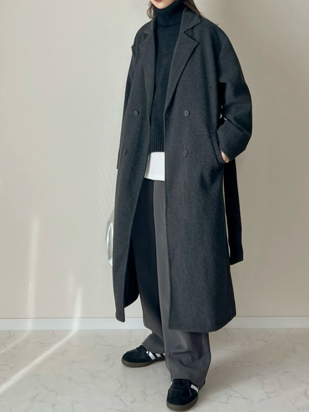 グレー系のチェスターコート、ブラック系のベスト、ブラック系のスニーカーを着用したレディースの冬コーディネートの3枚目の写真