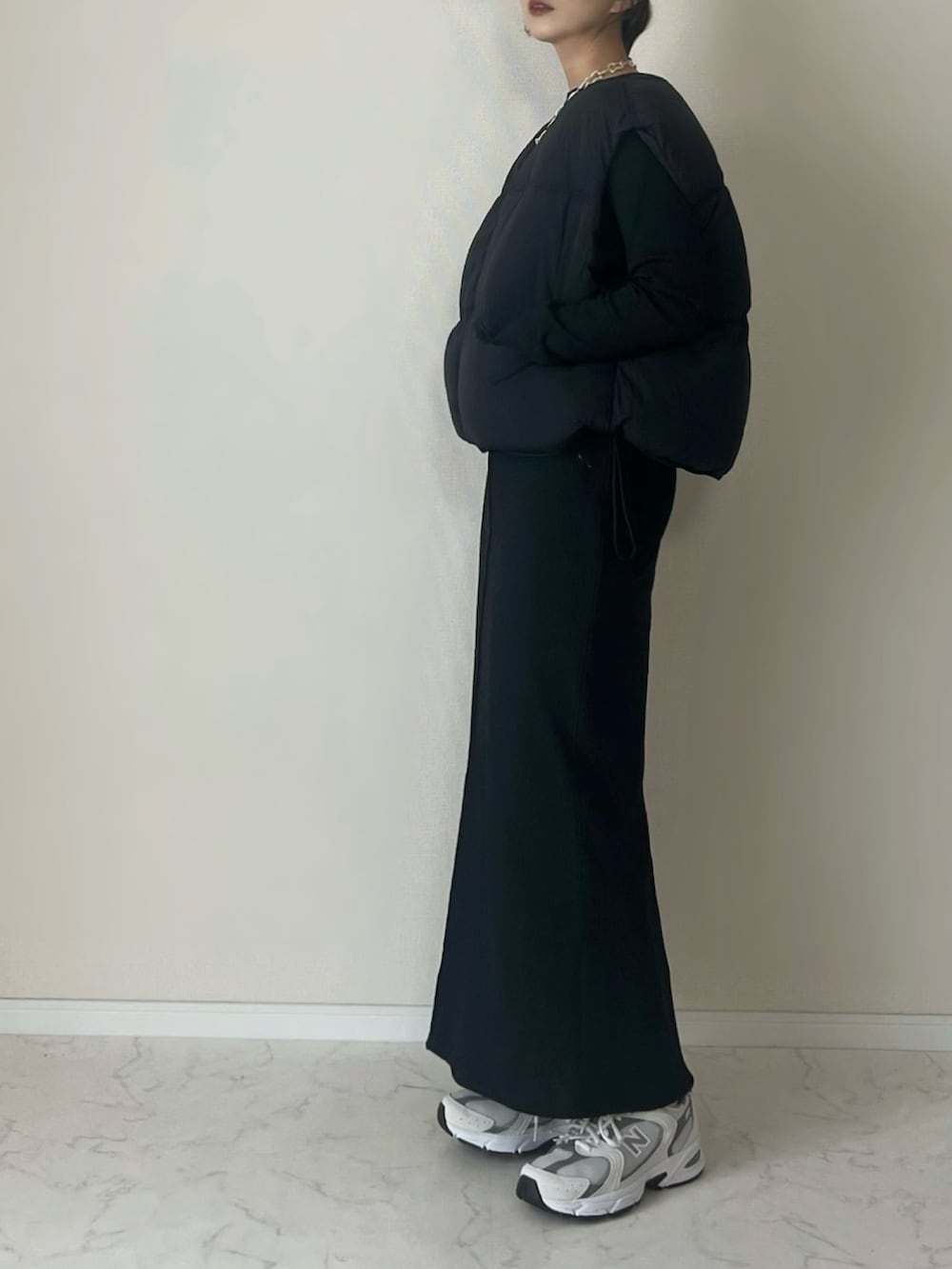 ブラック系のダウンベスト、グレー系のスニーカー、ブラック系のワンピース/ドレスを着用したレディースの冬コーディネートの2枚目の写真