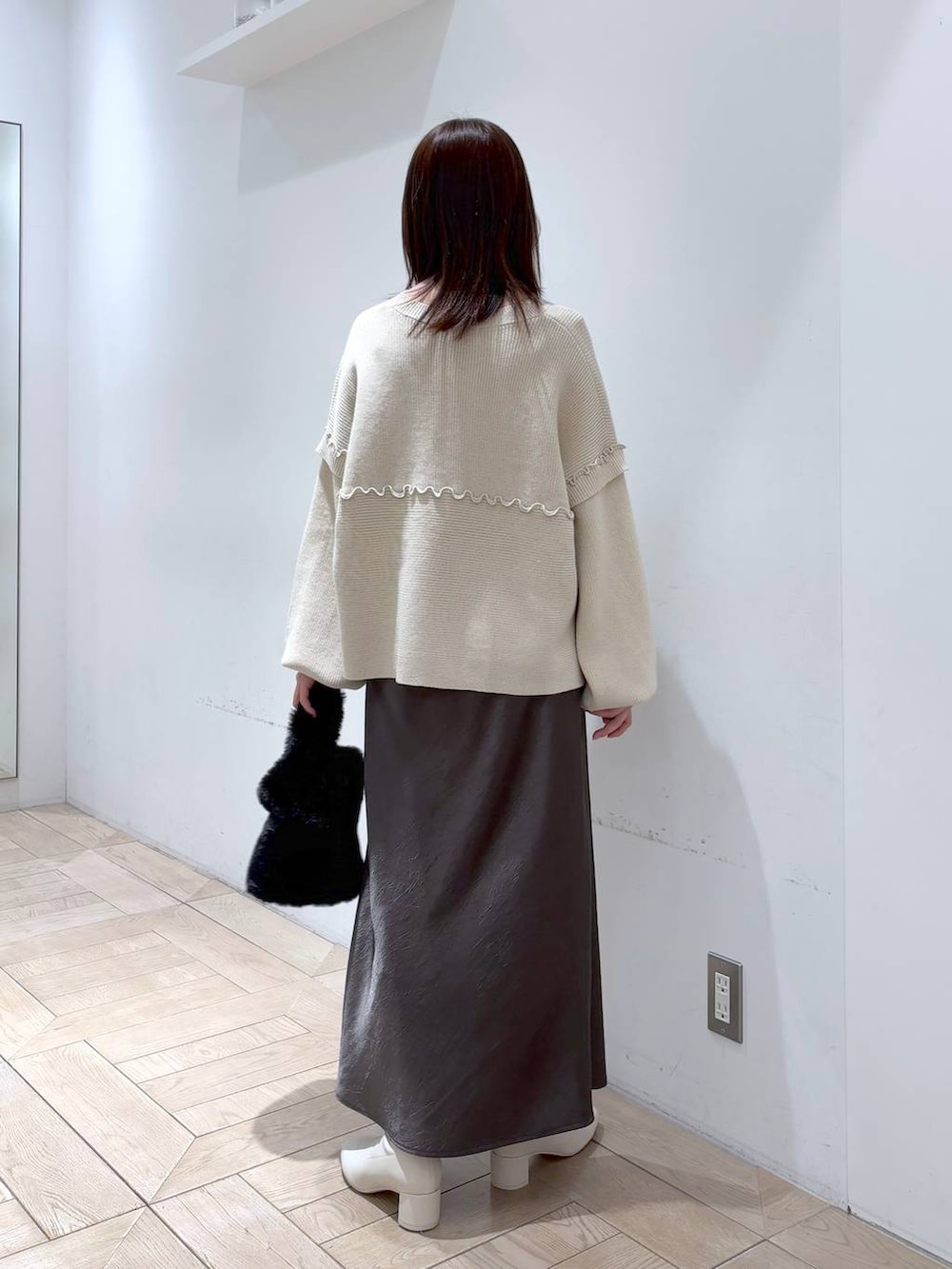 グレー系のスカート、ホワイト系のブーツ、ブラック系のショルダーバッグを着用したレディースの冬コーディネートの2枚目の写真