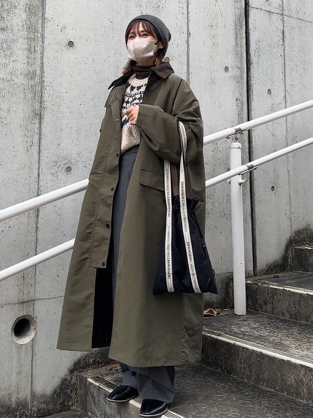 グリーン系のステンカラーコート、ブラック系のトートバッグ、ブラック系のニットキャップ/ビーニーを着用したレディースの冬コーディネートの3枚目の写真