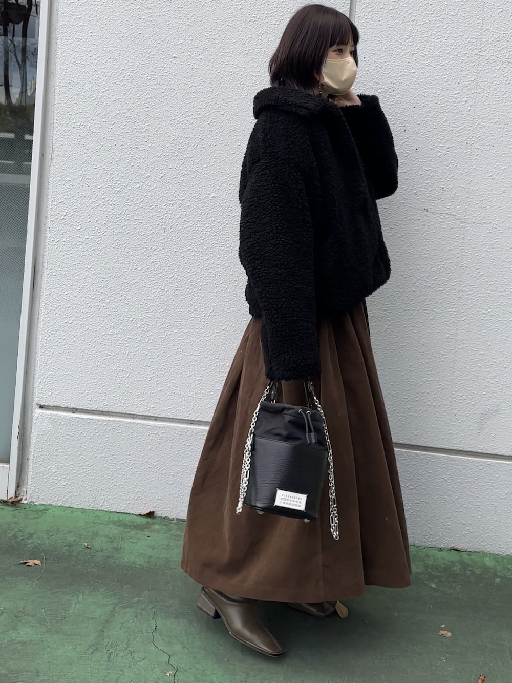 ブラック系のムートンコート、ブラウン系のワンピース、グリーン系のブーツを着用したレディースの冬コーディネートの2枚目の写真