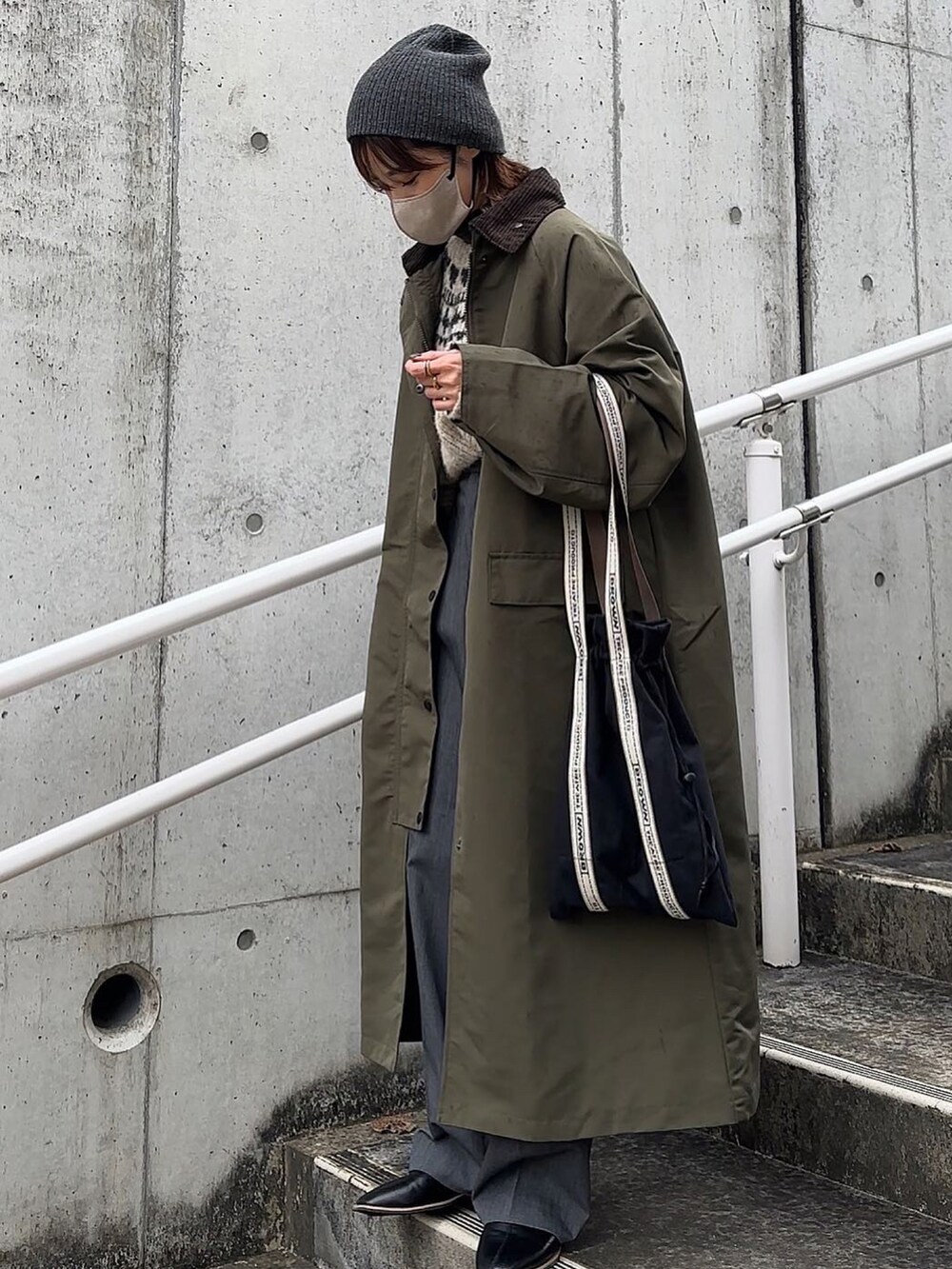 グリーン系のステンカラーコート、ブラック系のトートバッグ、ブラック系のニットキャップ/ビーニーを着用したレディースの冬コーディネートの2枚目の写真