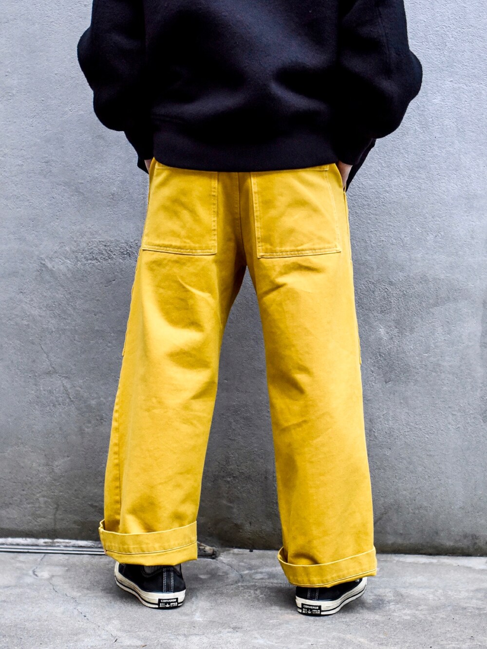 イエロー系のデニムパンツ、ブラック系のスニーカー、ブラック系のスタジャンを着用したメンズの秋コーディネートの3枚目の写真