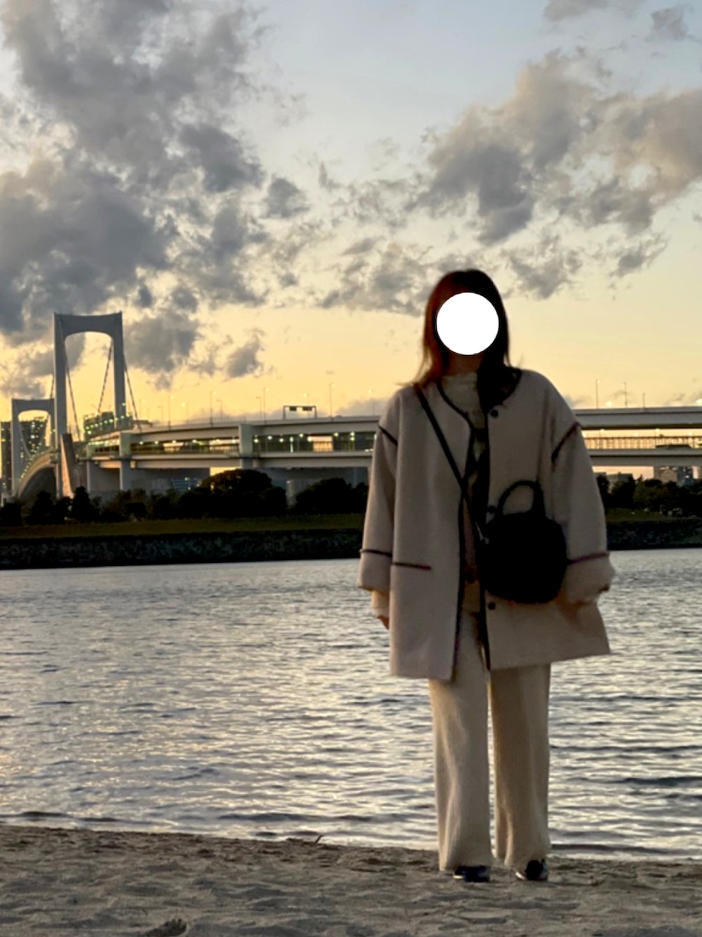 ベージュ系のノーカラーコート、ブラック系のショルダーバッグ、ベージュ系のニット/セーターを着用したレディースの冬コーディネートの2枚目の写真