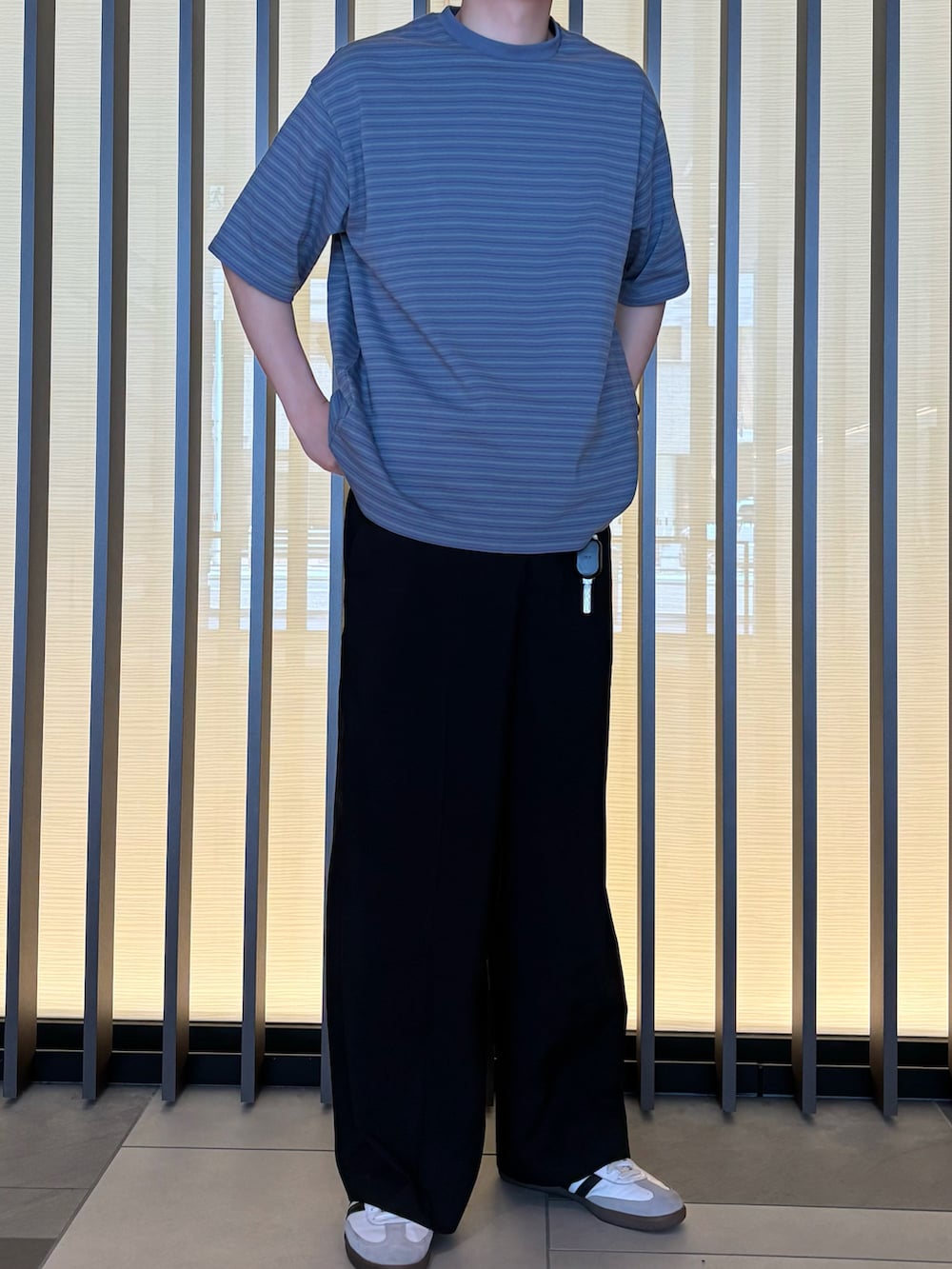 ブラック系のスラックス、ブルー系のTシャツ/カットソー、ホワイト系のスニーカーを着用したメンズの夏コーディネートの2枚目の写真