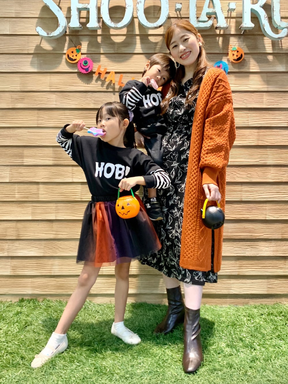 オレンジ系のカーディガン/ボレロ、ブラック系のワンピース、ブラウン系のブーツを着用したレディースの秋コーディネートの2枚目の写真