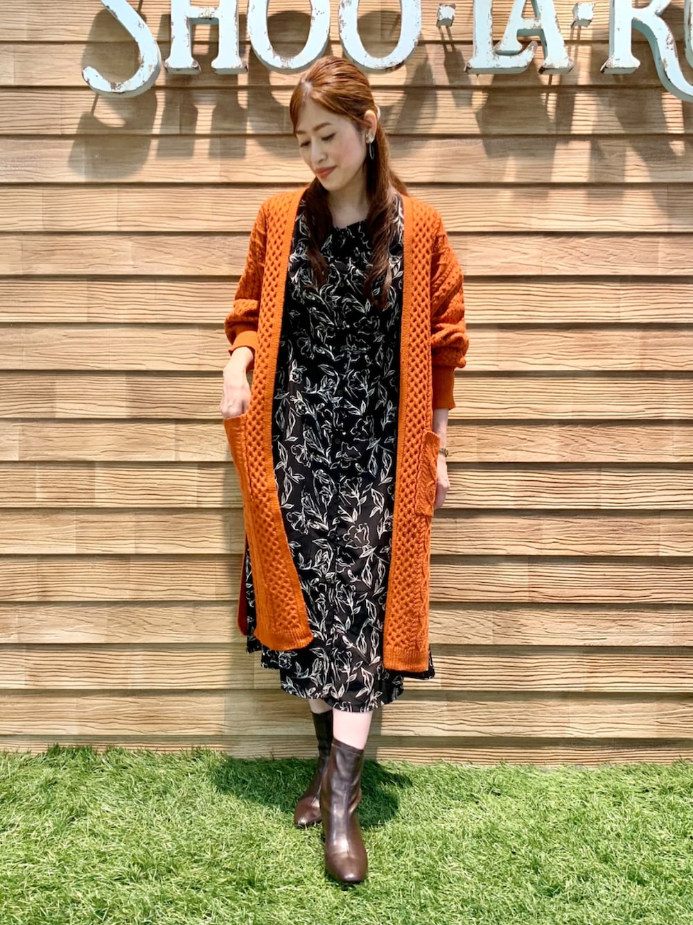 オレンジ系のカーディガン/ボレロ、ブラック系のワンピース、ブラウン系のブーツを着用したレディースの秋コーディネートの3枚目の写真