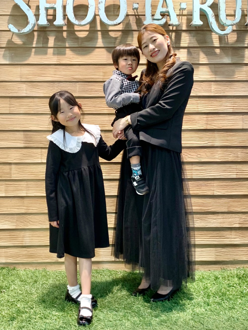 ブラック系のワンピース、ブラック系のドレスシューズ、ブラウン系のラッピングキットを着用したキッズの春コーディネートの2枚目の写真