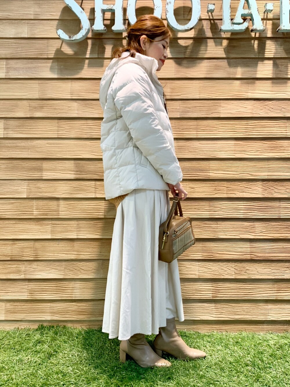 ホワイト系のダウンジャケット/コート、オレンジ系のニット/セーター、ホワイト系のスカートを着用したレディースの冬コーディネートの3枚目の写真