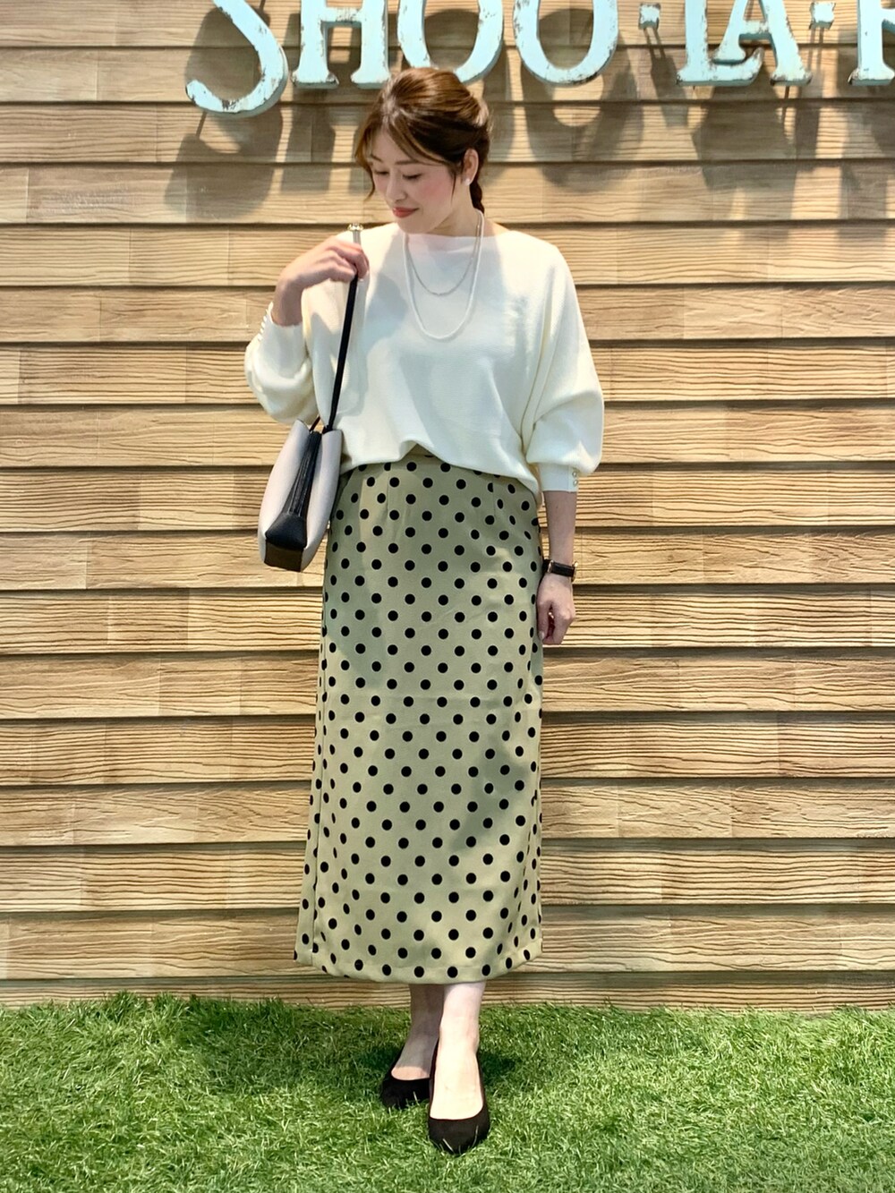 ホワイト系のニット/セーター、グリーン系のスカート、ブラック系のショルダーバッグを着用したレディースの春コーディネートの2枚目の写真